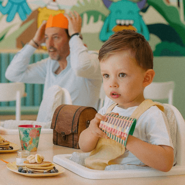 child eating with adult in background playing