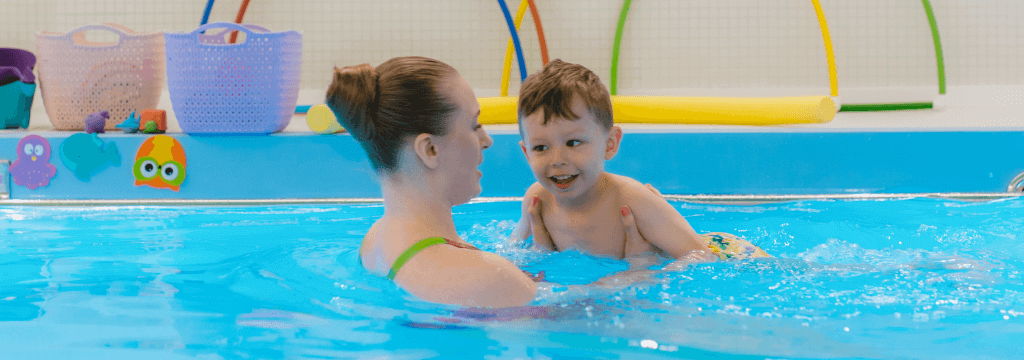 child swimming with teacher on tummy