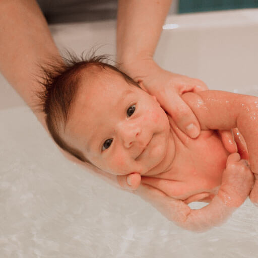 baby in woman's hands in tub in water