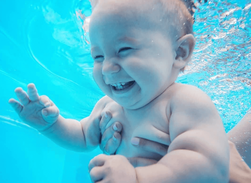 adult holding smiling baby underwater