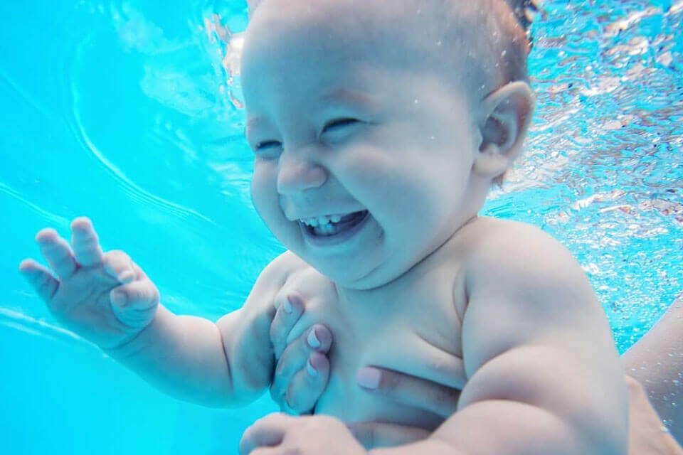 baby swimming underwater with smile being held by adult
