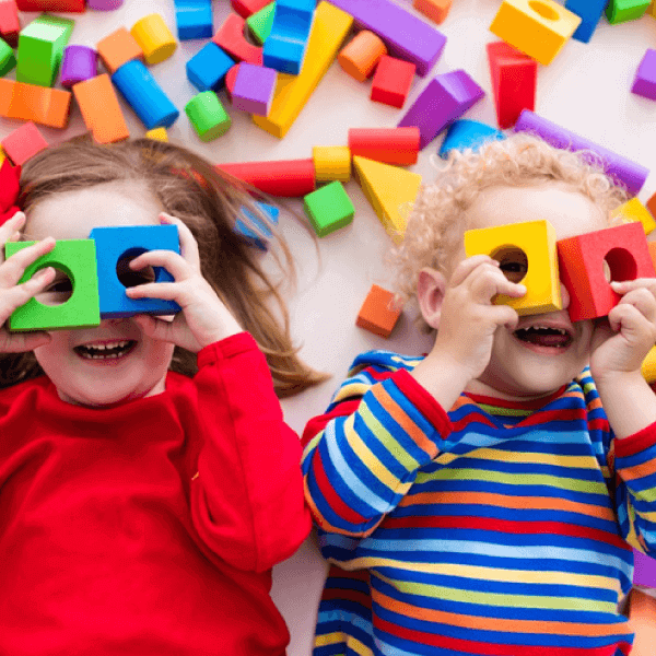 two children lying down looking through toy blocks
